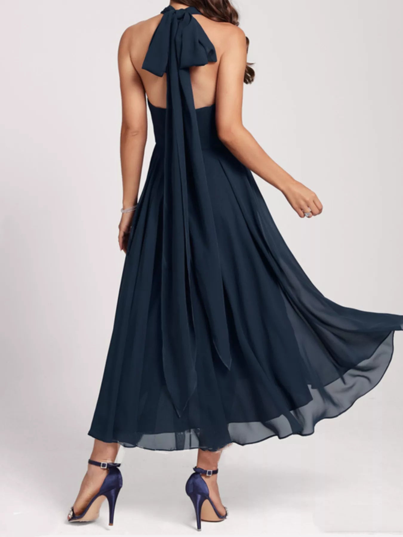 Navy blue halter neck dress with flowing fabric on a white background