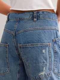 Close-up of blue jeans with a white top worn by a person.