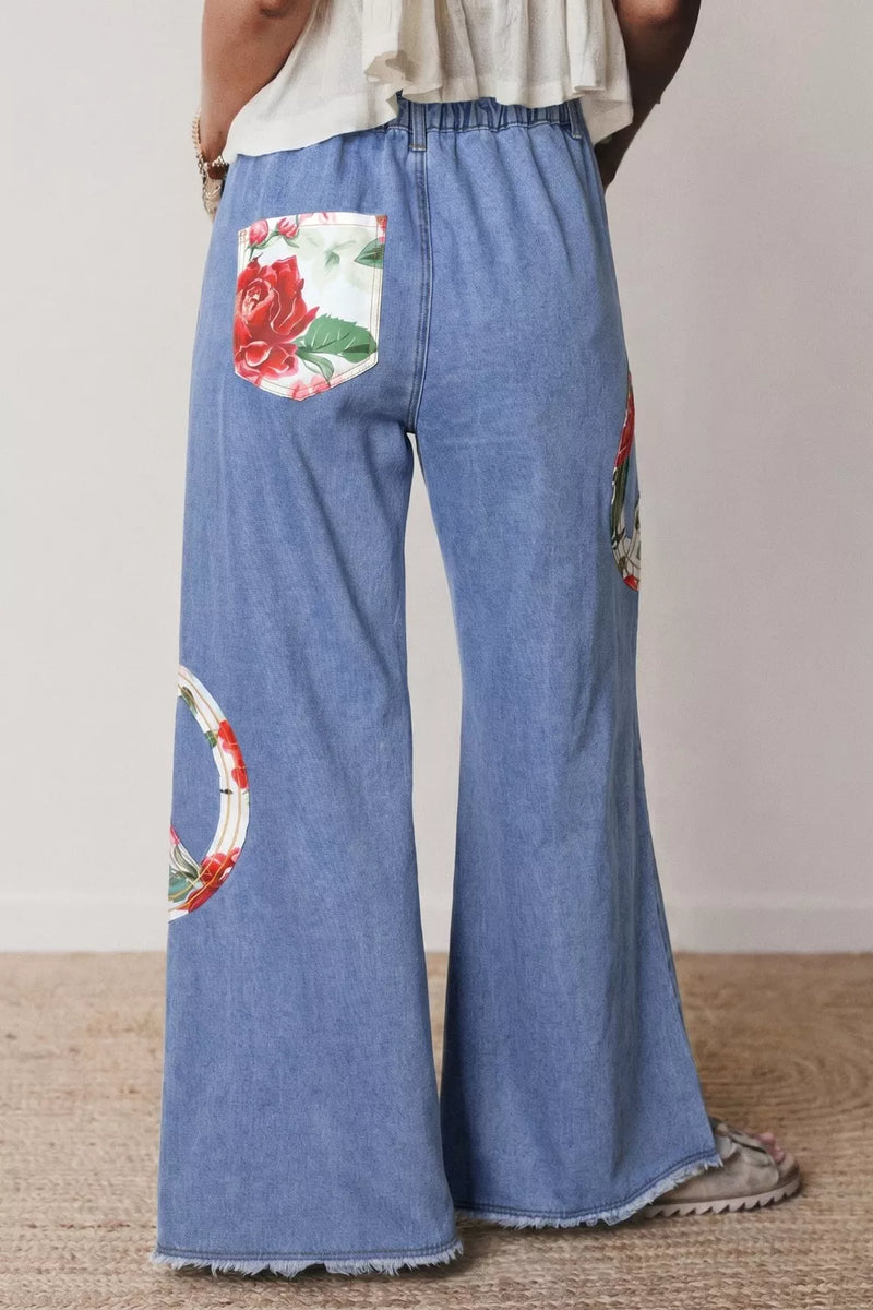 Blue denim pants with floral and geometric patterns worn by a person on a plain background