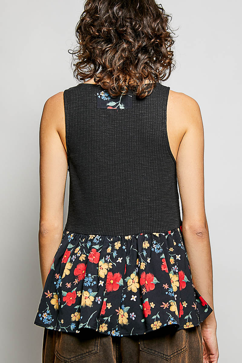 Person wearing a black sleeveless top with floral skirt on a plain background