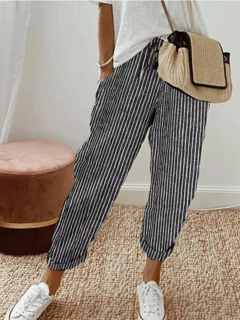 Person wearing striped pants and white sneakers with a beige bag indoors.