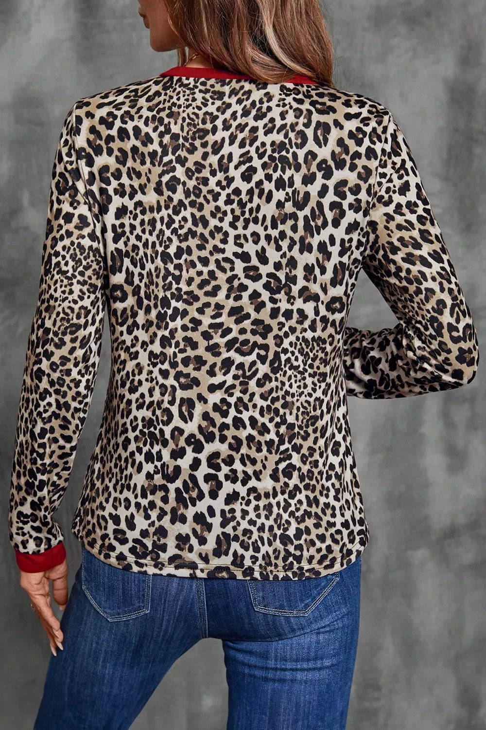 Person wearing a leopard print cardigan with red trim on a gray background