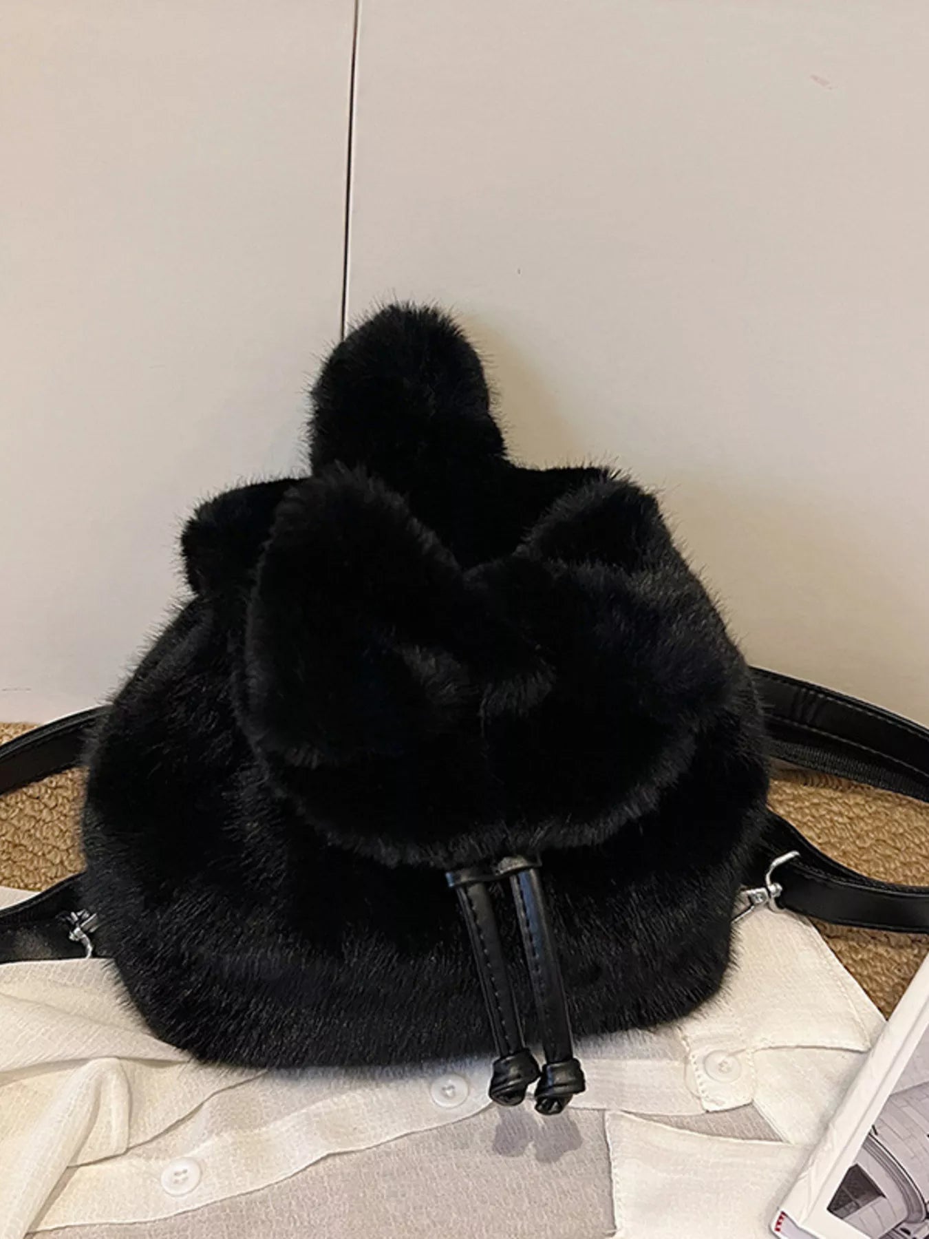 Black fluffy backpack on a light gray surface with a white background