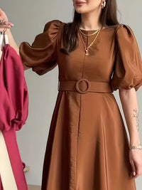 Woman wearing a brown dress with a belt, standing against a neutral background