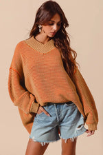 Woman wearing a mustard yellow sweater and denim shorts on a beige background