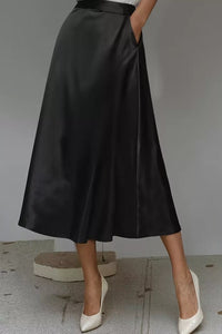 Person wearing a black satin skirt with white shoes on a neutral background