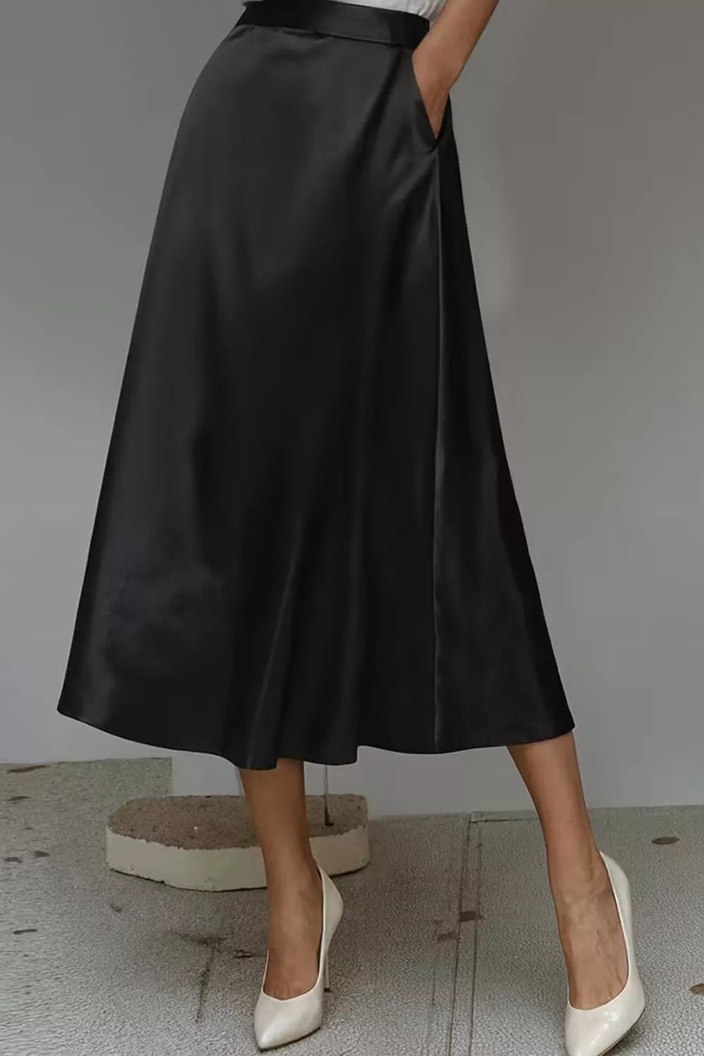 Person wearing a black satin skirt with white shoes on a neutral background