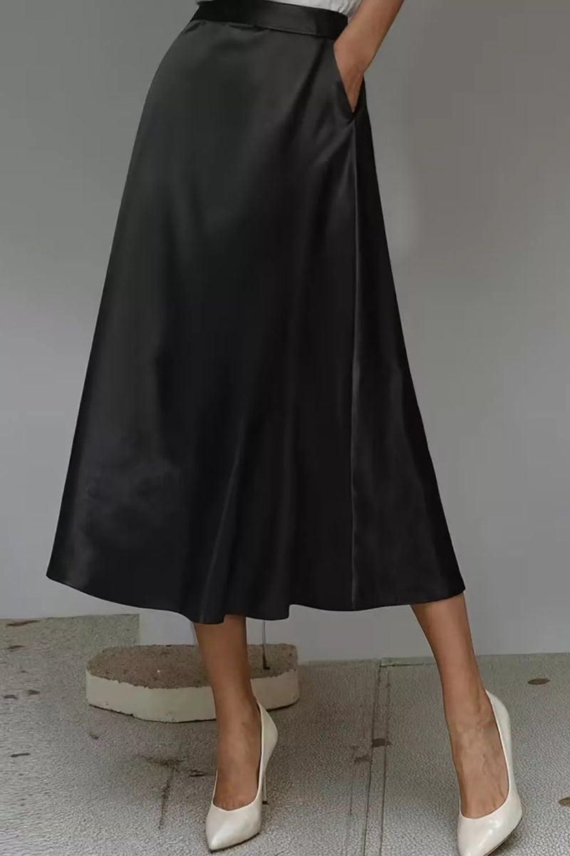 Person wearing a black satin skirt with white shoes on a neutral background