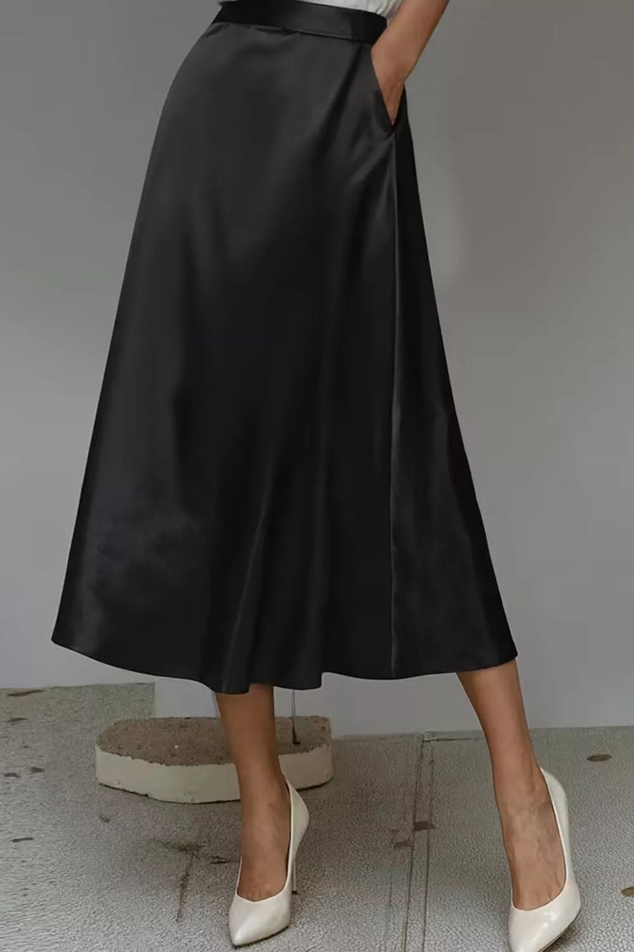 Person wearing a black satin skirt with white shoes on a neutral background
