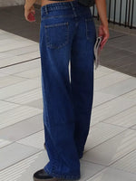 A person wearing wide-leg blue denim jeans, shown from the back in an outdoor setting with light-colored tiled flooring.
