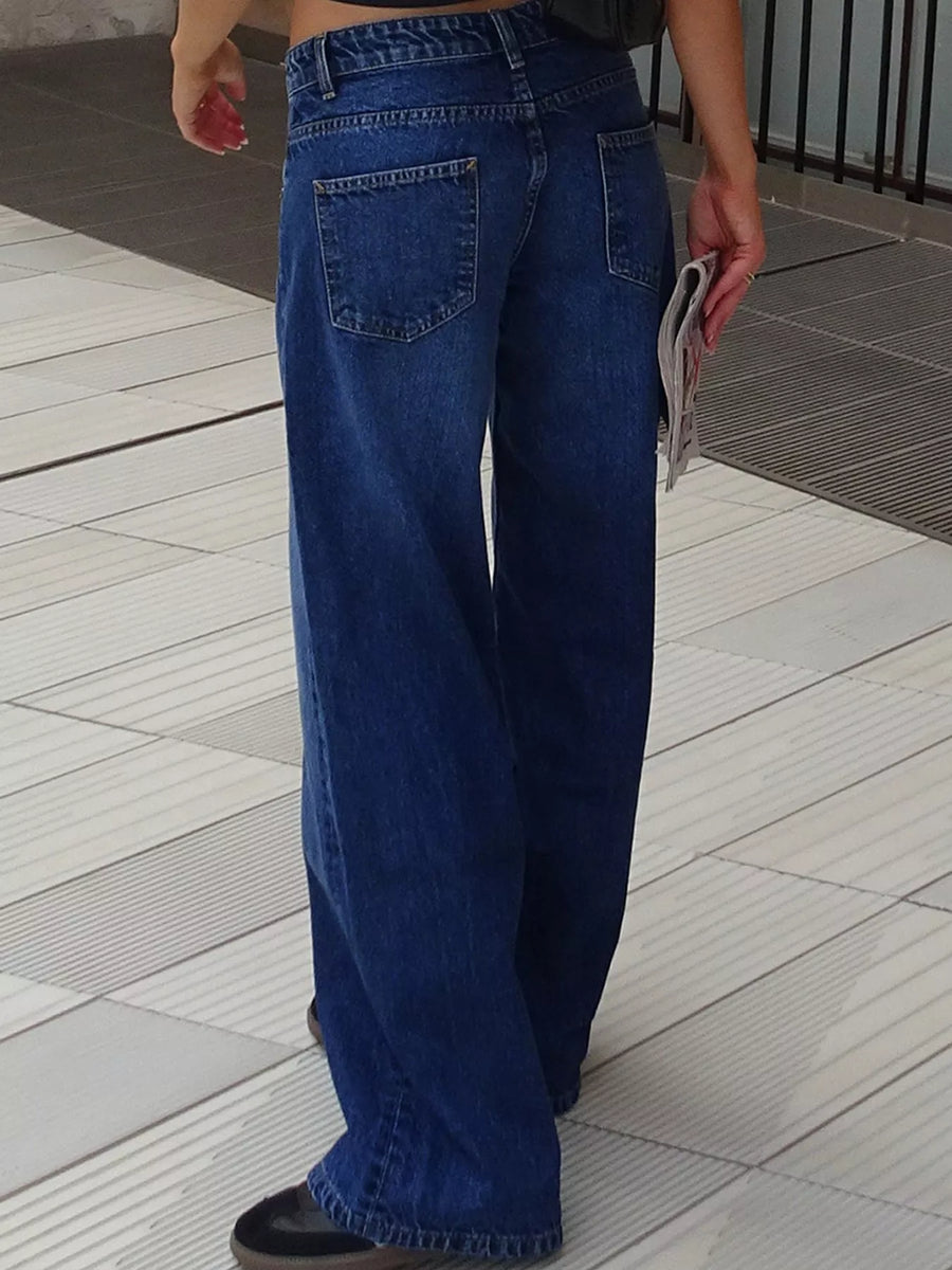 A person wearing wide-leg blue denim jeans, shown from the back in an outdoor setting with light-colored tiled flooring.