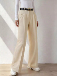 Person wearing beige wide-leg pants with a white shirt and black belt against a plain background