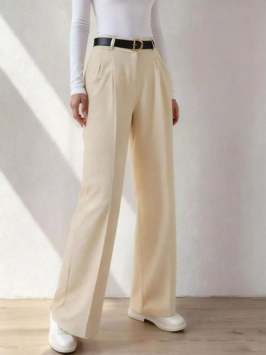 Person wearing beige wide-leg pants with a white shirt and black belt against a plain background