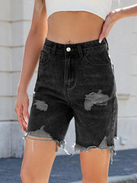 Black distressed denim shorts worn by a person with a blurred background