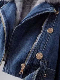 Close-up of a blue denim jacket with gold buttons and zipper, featuring a brand logo.