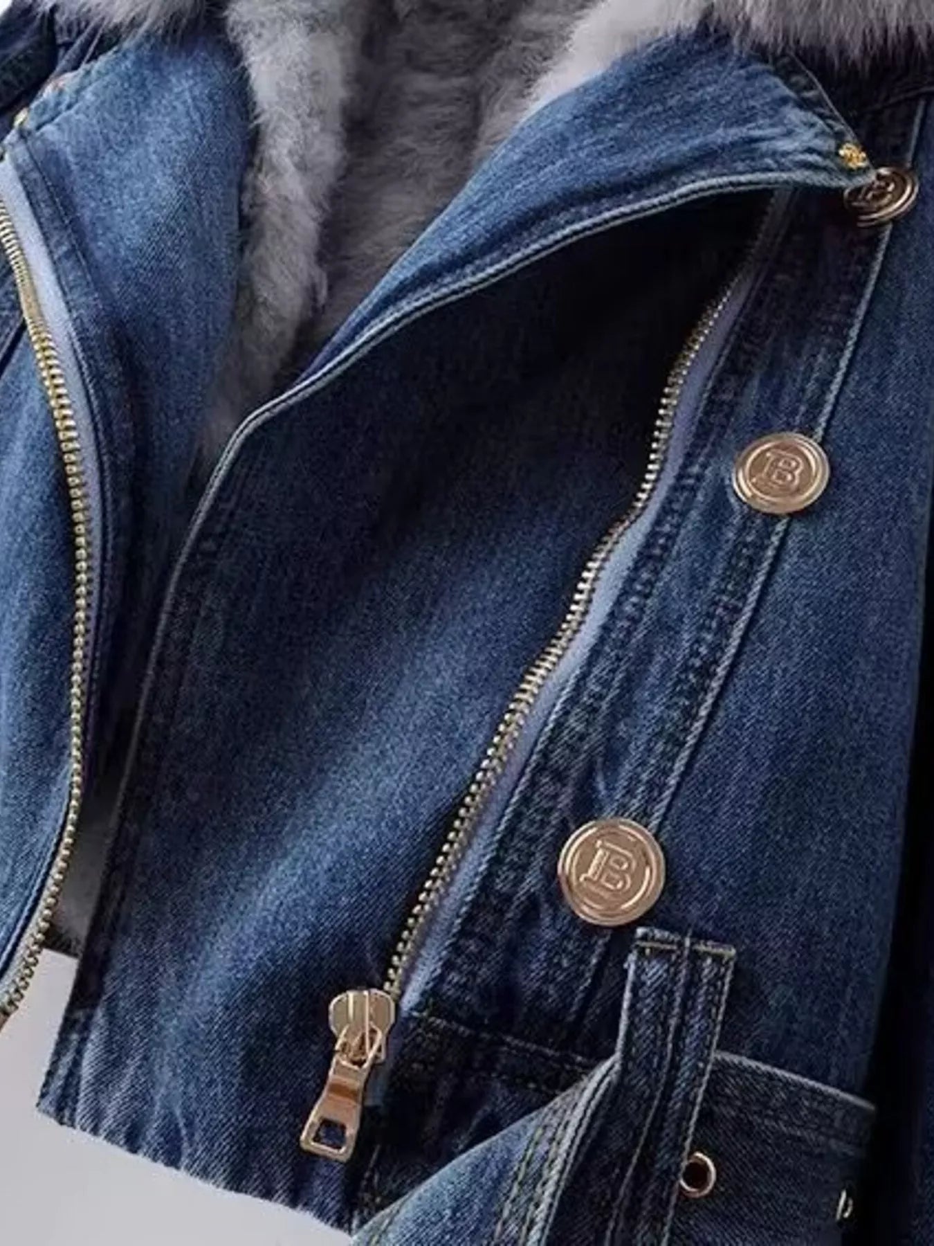 Close-up of a blue denim jacket with gold buttons and zipper, featuring a brand logo.