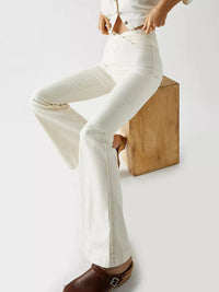 Person wearing white flared pants sitting on a wooden block against a white background