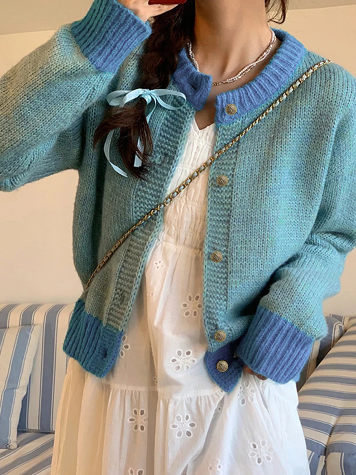 Person wearing a blue knitted cardigan over a white dress with a striped couch in the background.