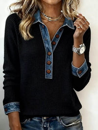 Person wearing a black sweater with denim collar and cuffs on a plain background