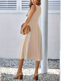 Woman wearing a beige sleeveless dress holding a clutch against a white background.