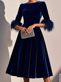 Navy blue dress with feathered sleeves held by a hand with a silver clutch against a neutral background
