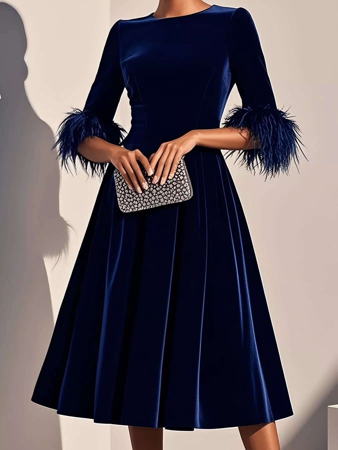 Navy blue dress with feathered sleeves held by a hand with a silver clutch against a neutral background