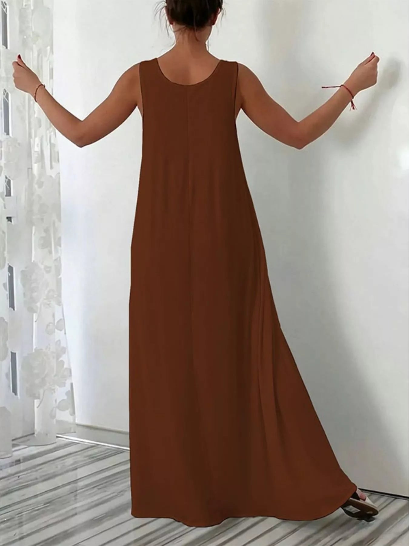 Brown sleeveless dress worn by a person against a white wall.