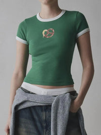 Person wearing a green t-shirt with a logo and jeans, holding a gray sweater against a plain background