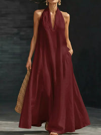 Woman wearing a burgundy halter neck dress holding a woven bag against a dark background