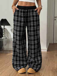 Person wearing black plaid pants in a room with a lamp and door in the background.