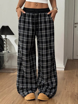 Person wearing black plaid pants in a room with a lamp and door in the background.