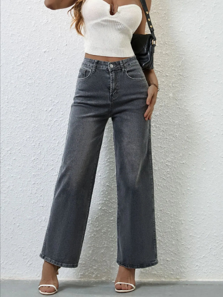 Person wearing high-waisted dark jeans and a white top against a light gray background