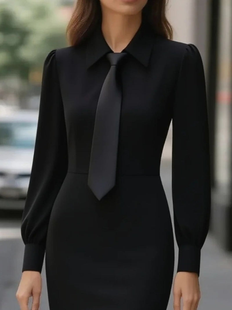 Person wearing a black dress with a tie in an urban setting