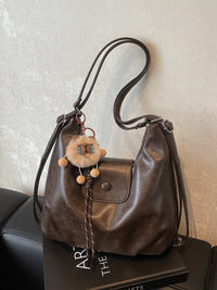 Brown leather handbag with a decorative keychain on a textured surface