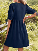 Woman wearing a navy blue dress in a natural setting with greenery and flowers.