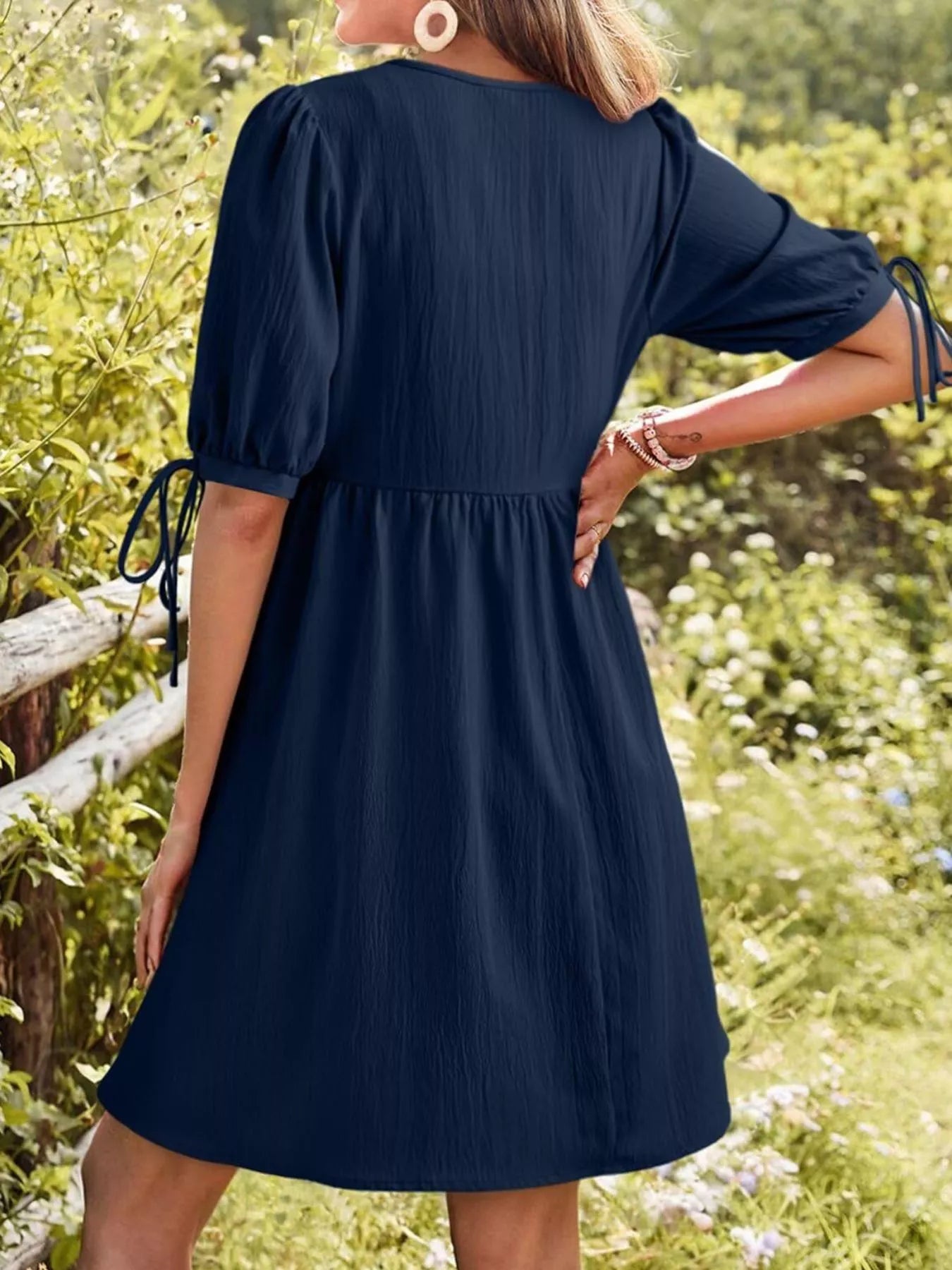 Woman wearing a navy blue dress in a natural setting with greenery and flowers.
