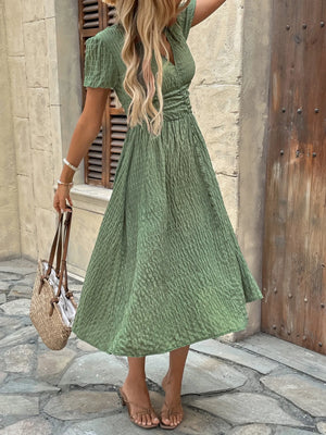 Woman wearing a green dress standing on a stone pavement.