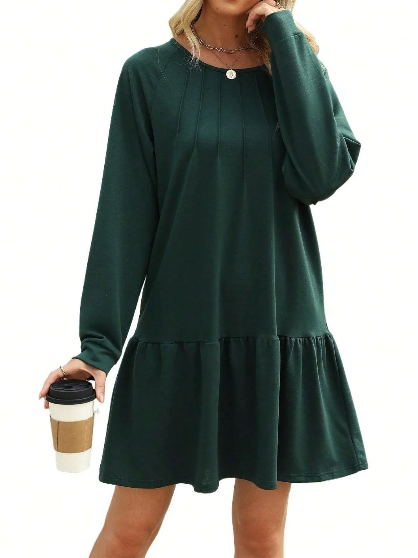 Green dress with long sleeves and ruffled hem worn by a person holding a coffee cup on a white background