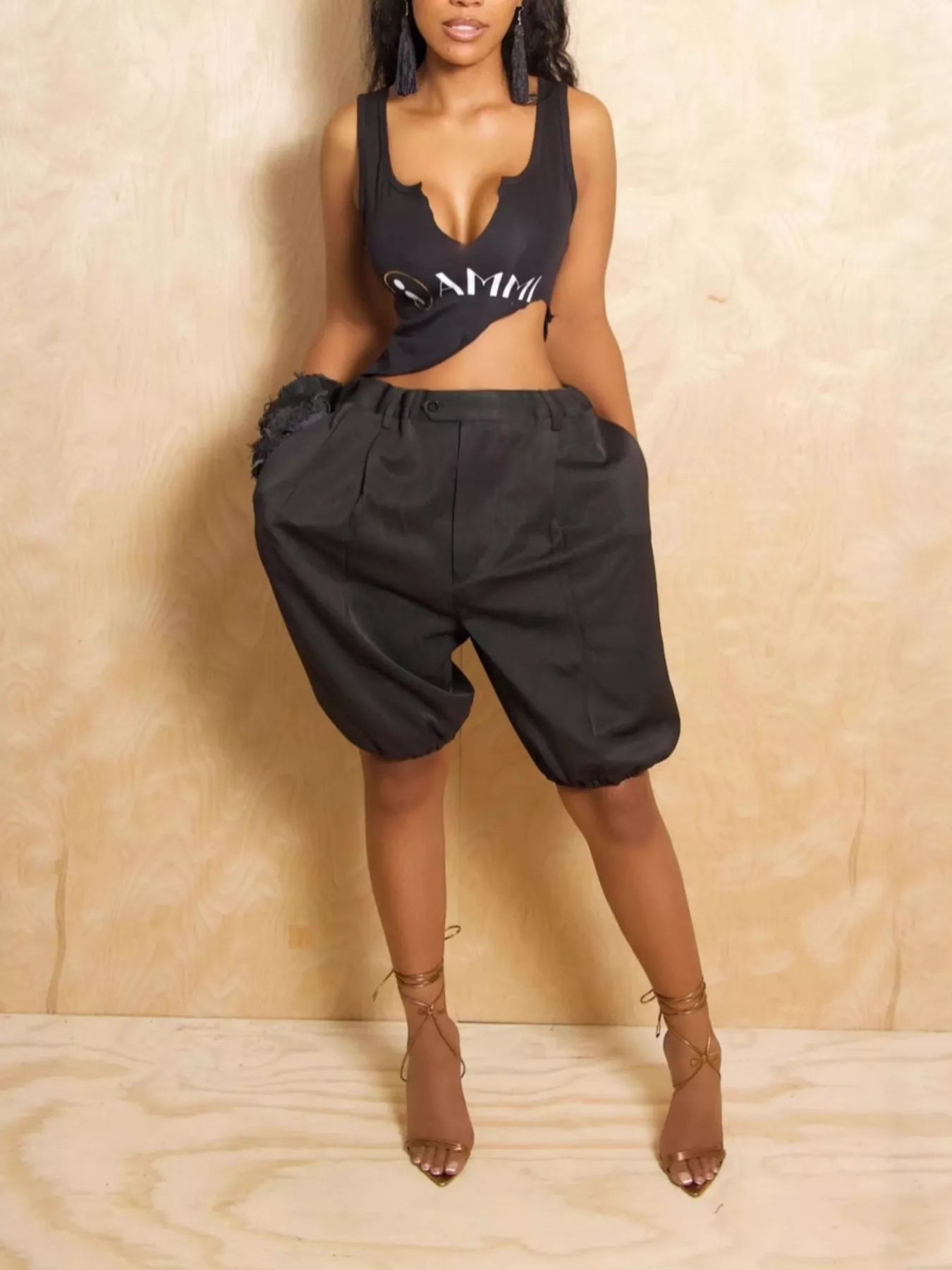Woman wearing a black tank top and shorts against a beige wall.