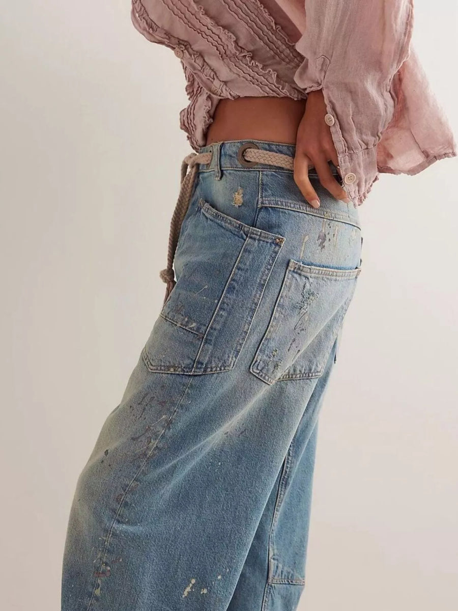 Person wearing a light pink blouse and blue jeans on a plain background