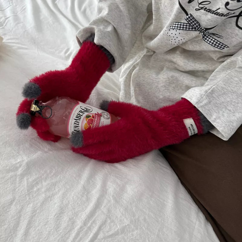 Person wearing red fuzzy gloves holding a bottle of Smirnoff Vodka on a bed.