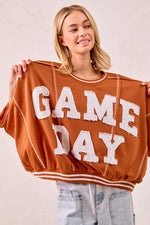 Woman holding up a 'GAMEDAY' sweatshirt against a plain background