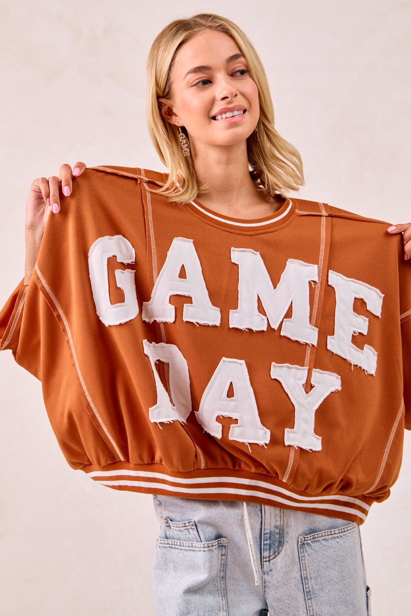Woman holding up a 'GAMEDAY' sweatshirt against a plain background
