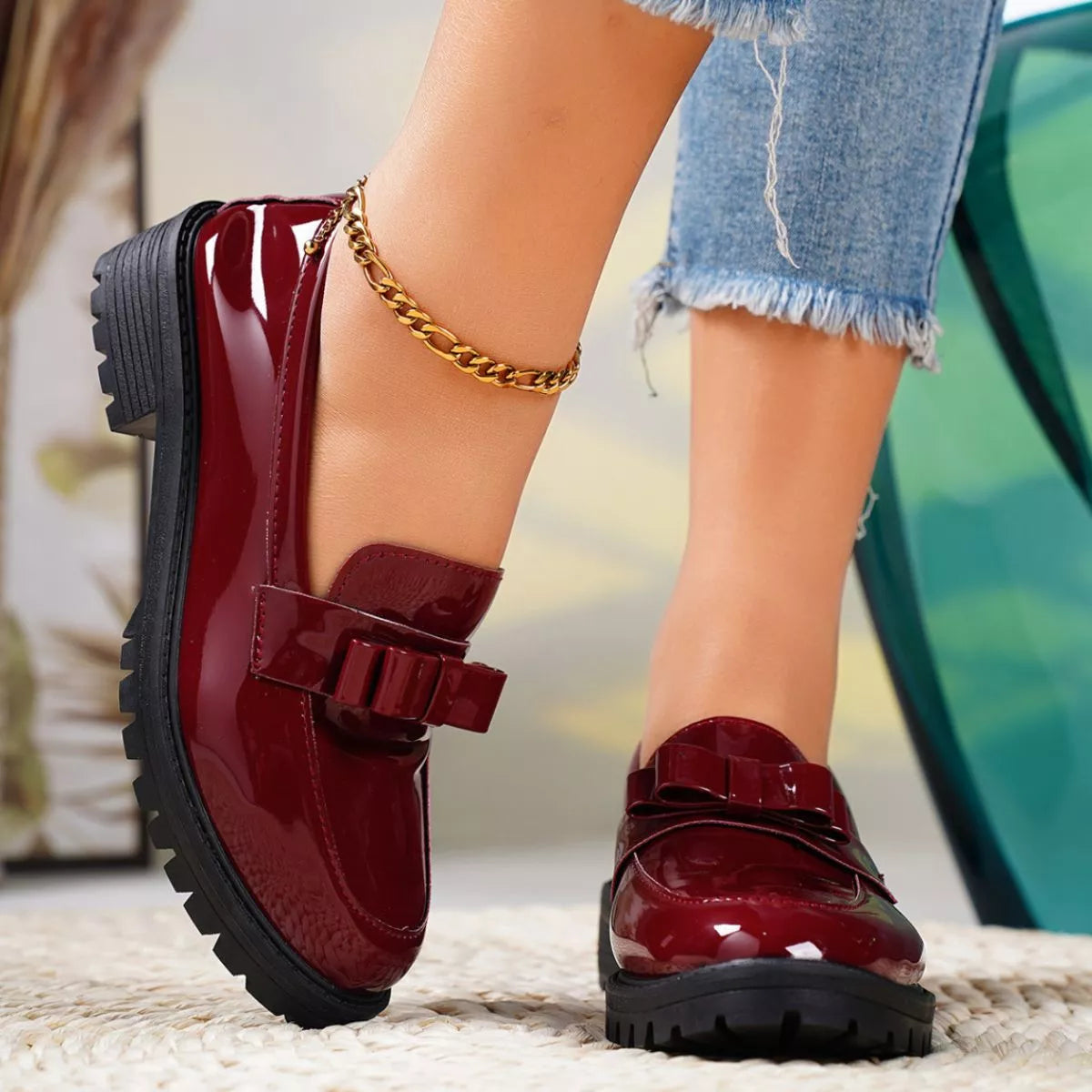 Red patent leather shoes with black soles worn by a person, with a blurred background.