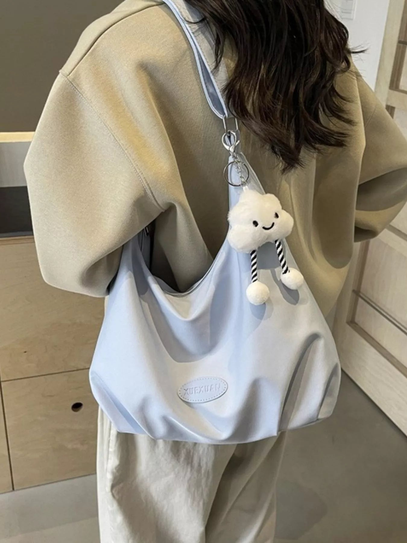 Person wearing a beige hoodie with a light blue bag featuring a cloud charm.