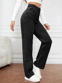 Person wearing black high-waisted jeans and white sneakers in a minimal indoor setting.