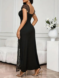 Woman wearing a black evening gown with sheer sleeves in a room with white walls and furniture.