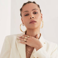 A woman wearing four gold rings on her finger and 2.5" Skylar Hoops in her ears