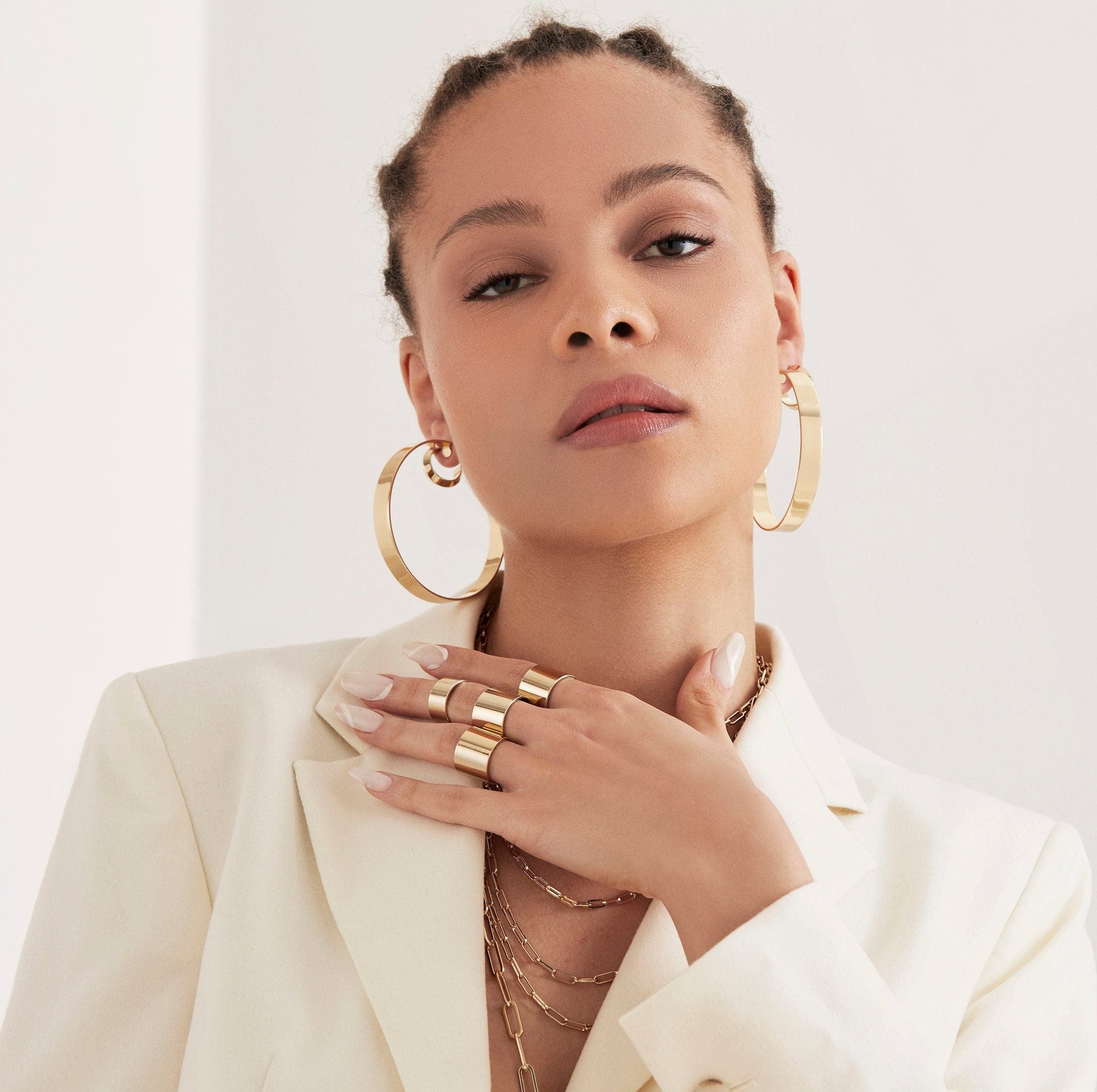 A woman wearing four gold rings on her finger and 2.5" Skylar Hoops in her ears