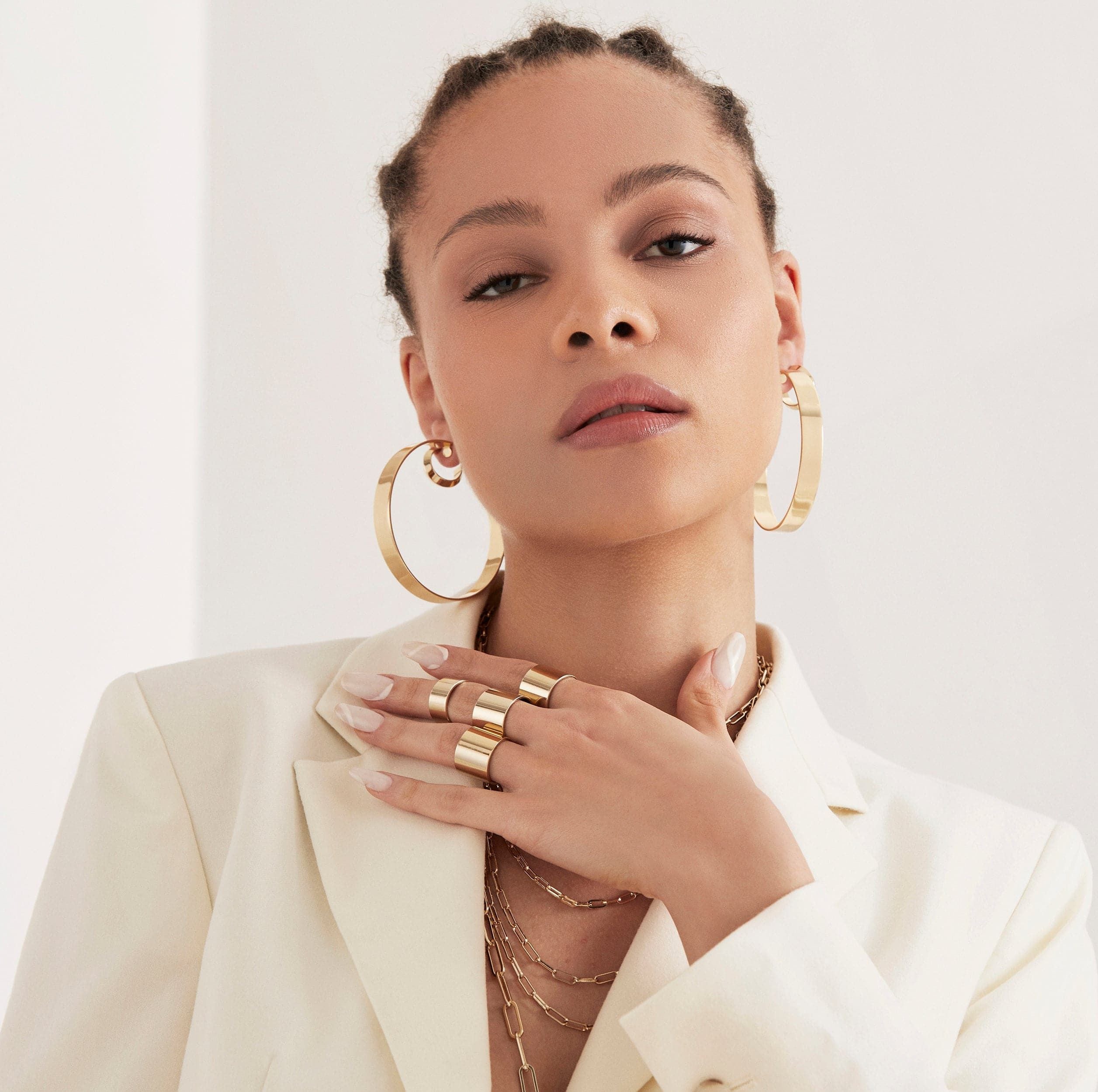 A woman wearing four gold rings on her finger and 2.5" Skylar Hoops in her ears